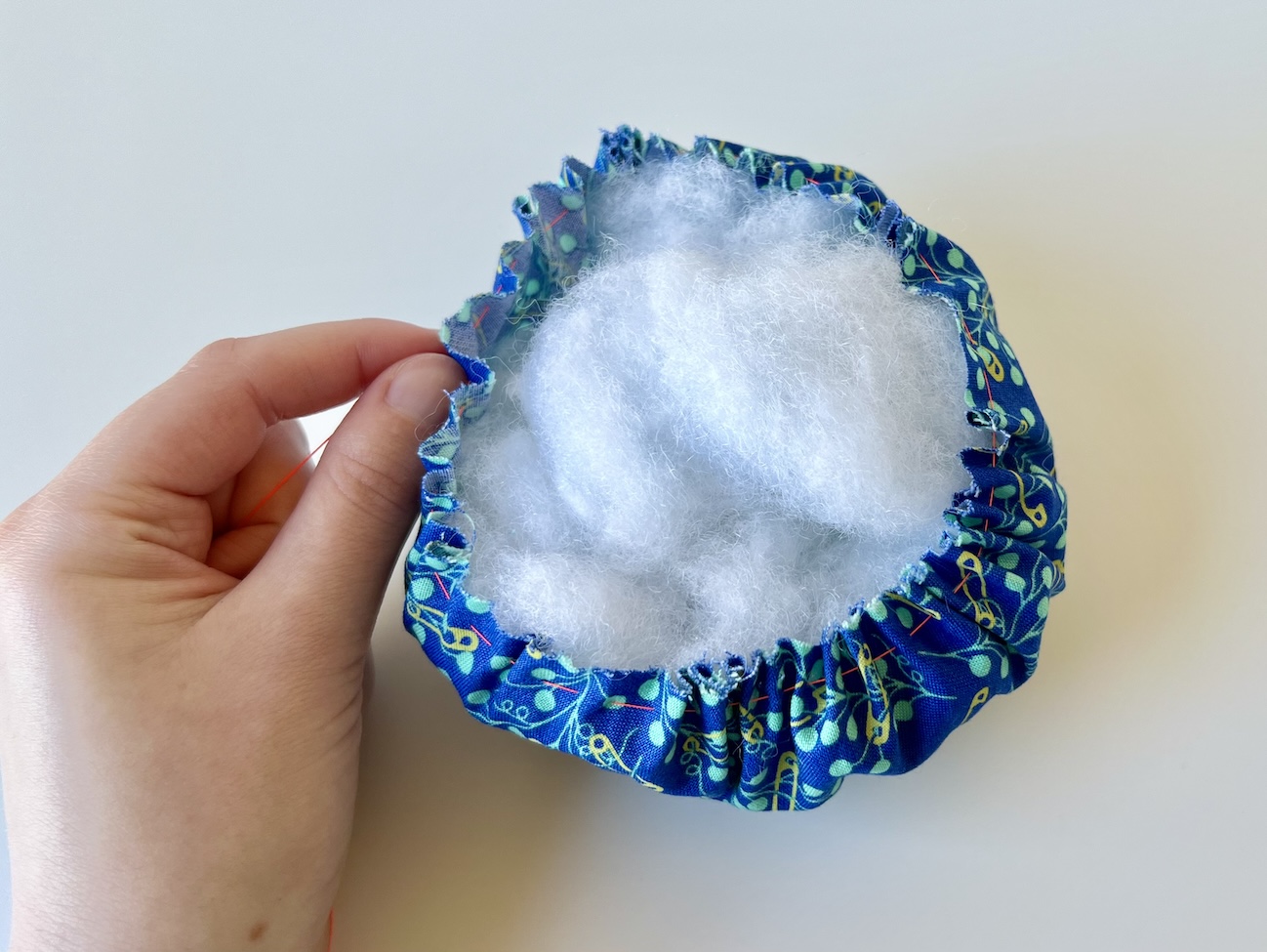 A hand holding a gather circle of fabric stuffed with fiber fill