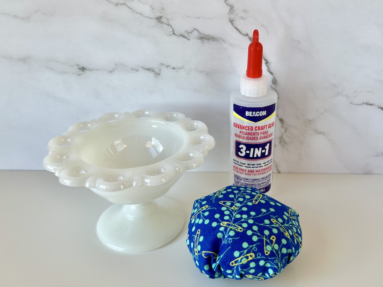 A candy dish, a bottle of Beacon 3-in-1 glue, and a fabric pincushion