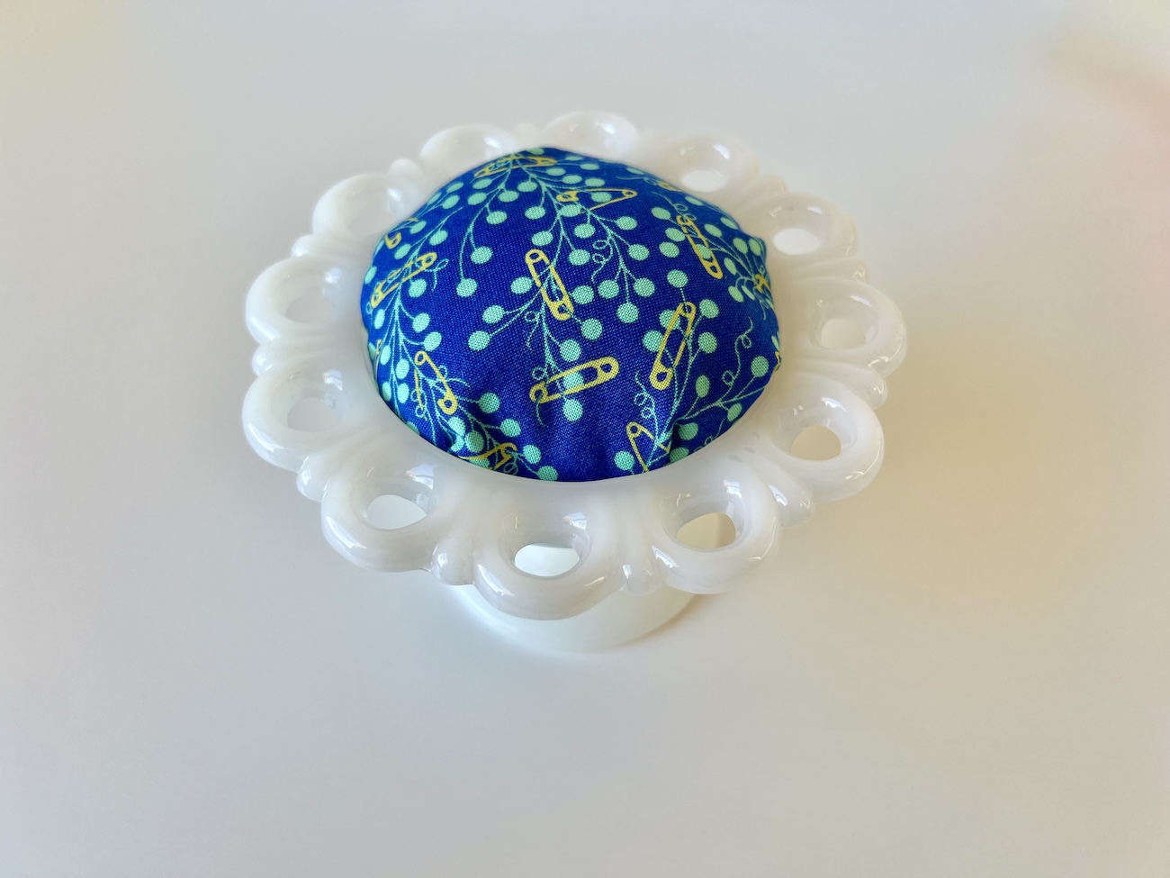 A white, milk glass candy dish with a blue fabric pincushion top