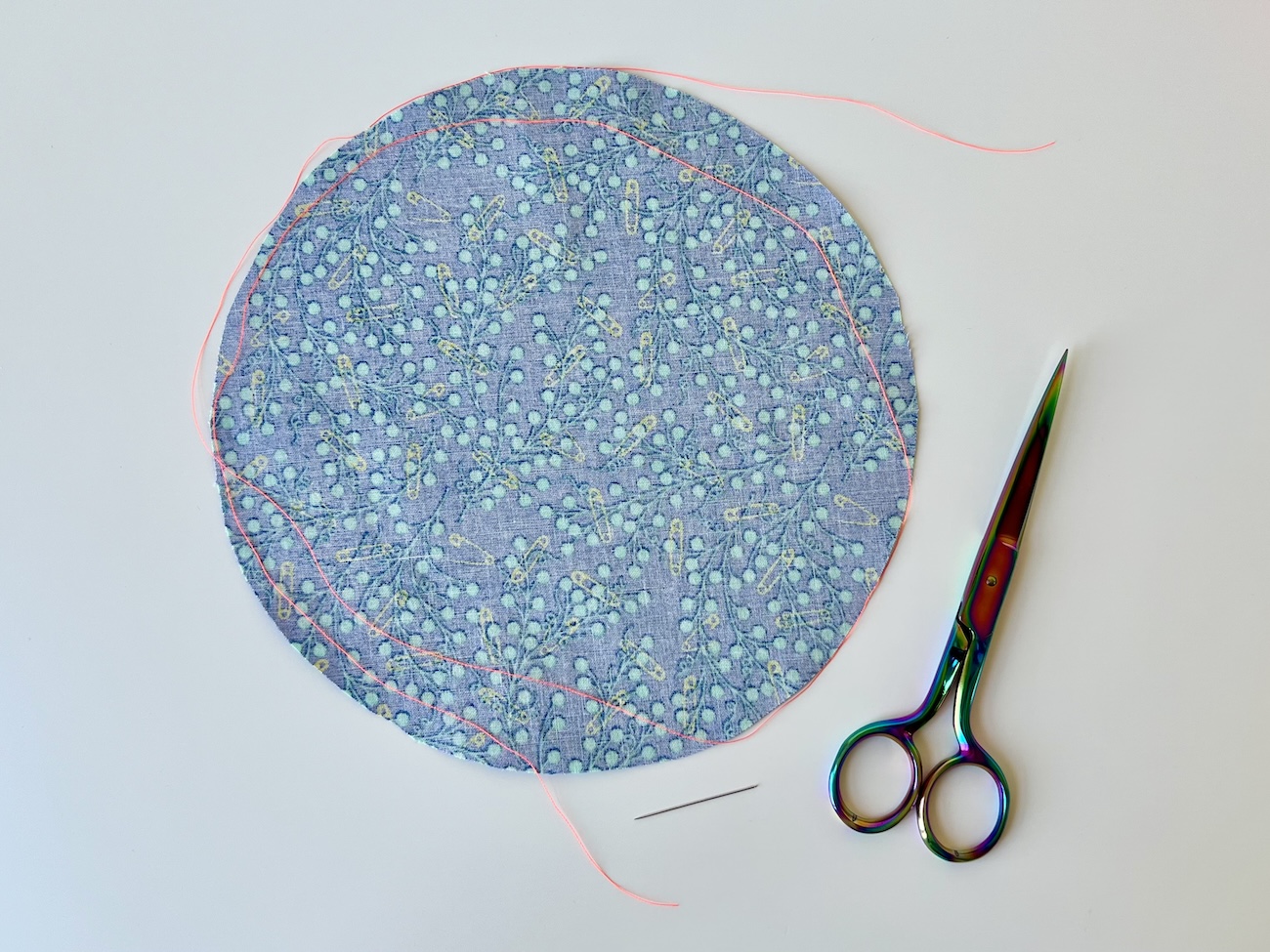 A circle of fabric, a long piece of thread, a hand sewing needle, and a pair of scissors